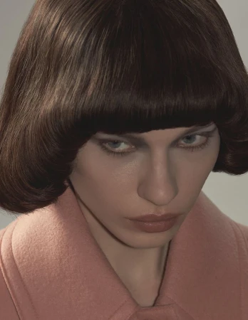 Close-up portrait of model Kate Letskaya with a blunt brunette bob hairstyle wearing a dusty pink wool coat.