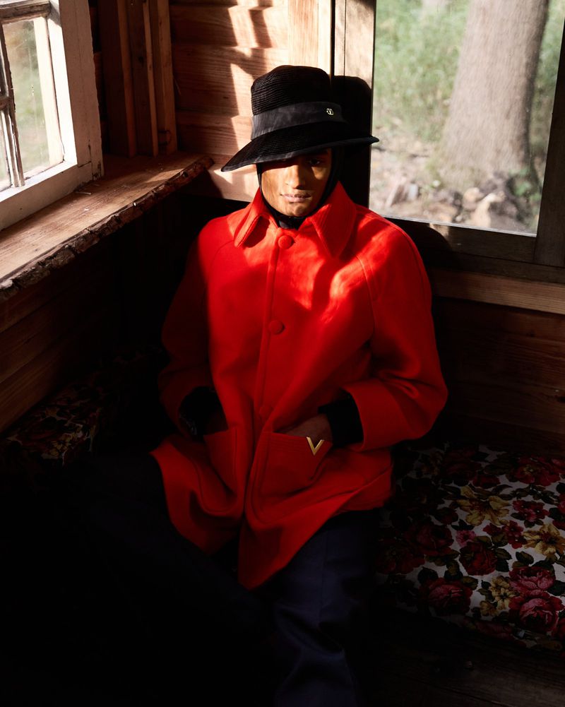 Person in red coat and black hat sitting in rustic cabin with natural light streaming through window in a medium interior shot.