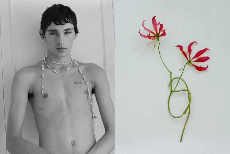 Black and white image of a shirtless young male wearing pearl necklaces alongside a pair of red and green glory lily flowers.