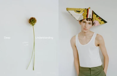 Model Noah Bates in a white tank top with a folded patterned scarf hat beside a dried flower stem against a white backdrop.