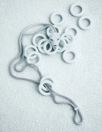 Animal-shaped pendant on a silver chain, surrounded by many white rings on a textured white background. Jewelry product shot.