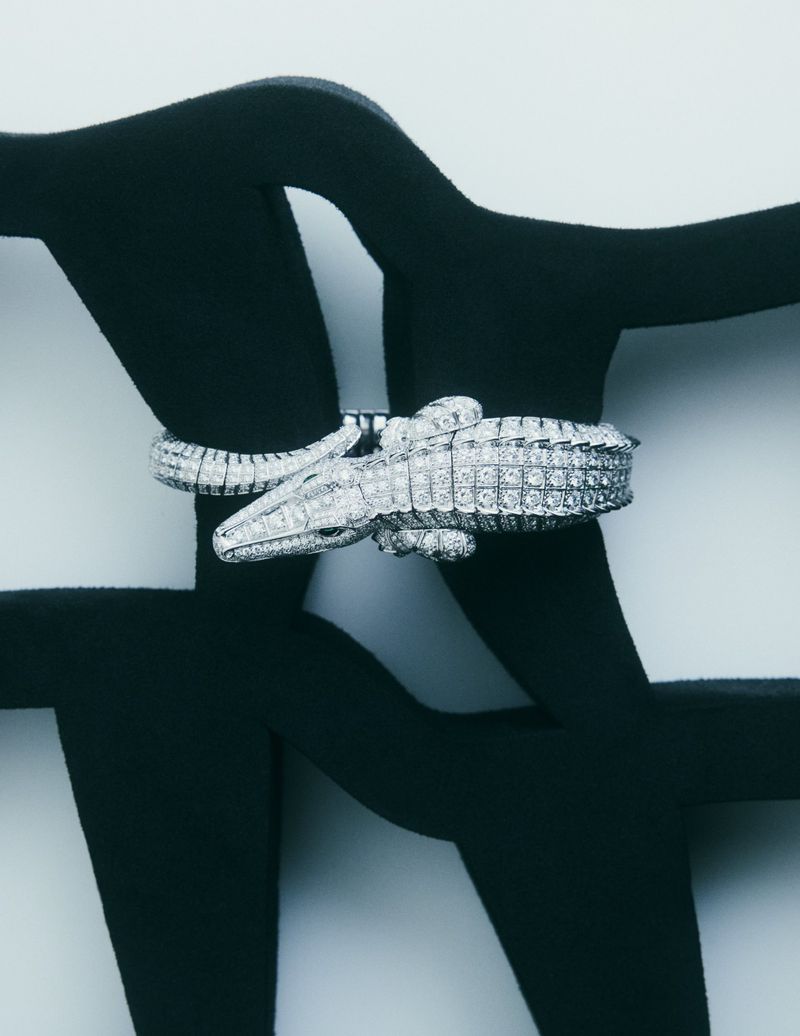 Statement fashion jewelry shot featuring a diamond crocodile bracelet wrapped around a black abstract metal sculpture on white.