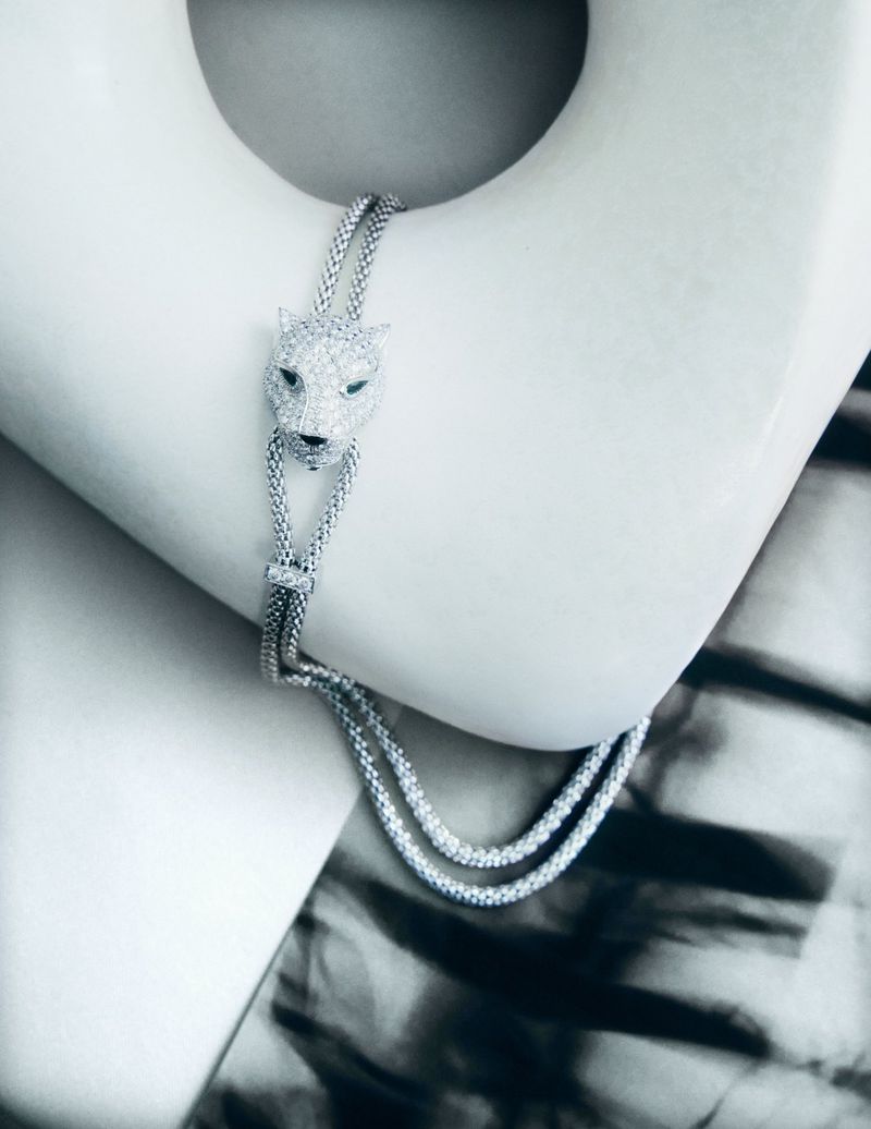 Close-up of a white gold panther head bracelet with green gemstone eyes. The bracelet is draped on a curved white surface.