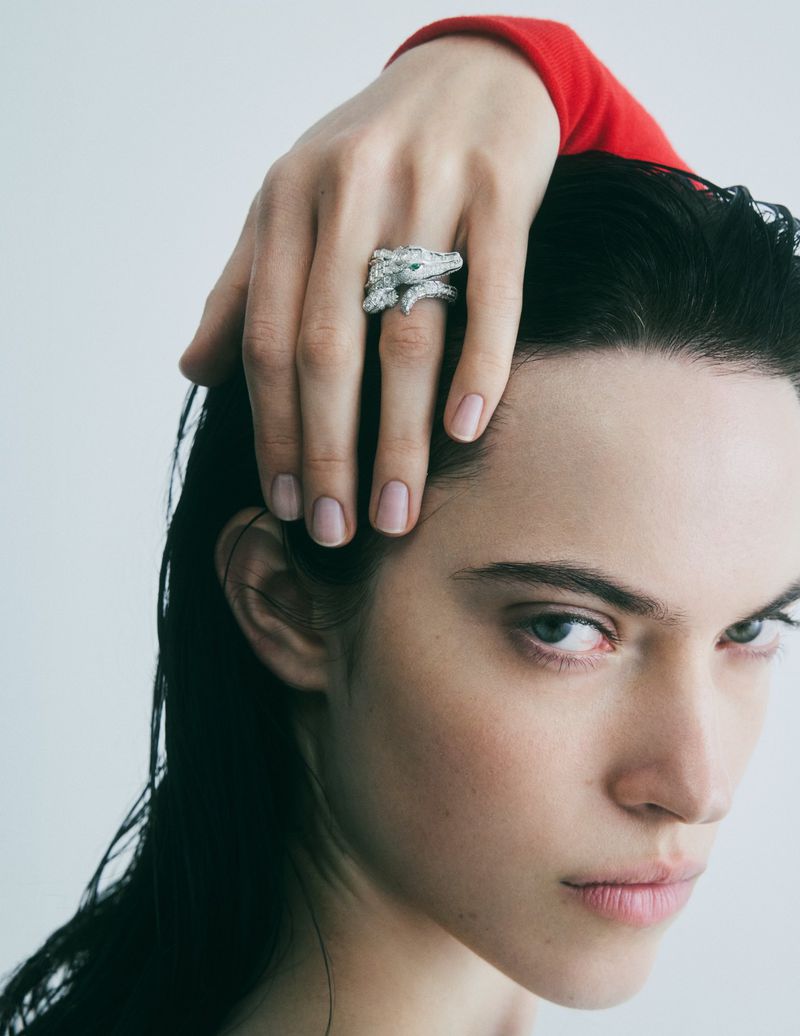 Close-up studio shot of a young woman with silver animal ring on her finger. The image has a soft, neutral color palette.