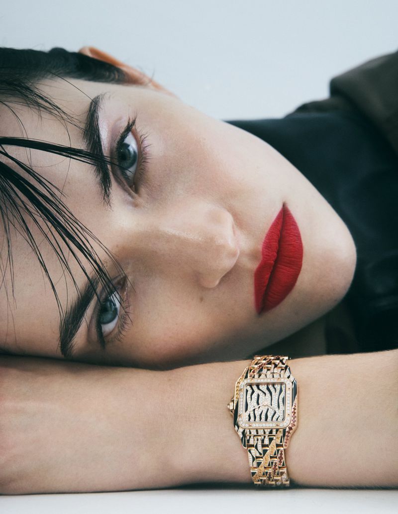 Close-up of a model with red lipstick and a designer watch. The image is shot in a bright, neutral studio setting for a jewelry advertisement.