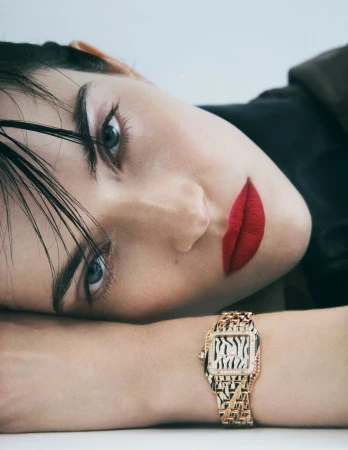 Close-up of a model with red lipstick and a designer watch. The image is shot in a bright, neutral studio setting for a jewelry advertisement.