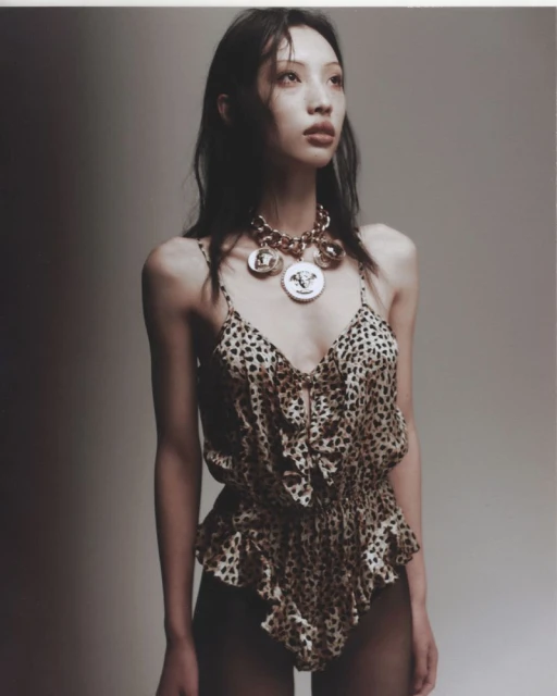Portrait of a young Asian woman with dark hair wearing a leopard-print top and gold necklace in a photo studio with diffused lighting.
