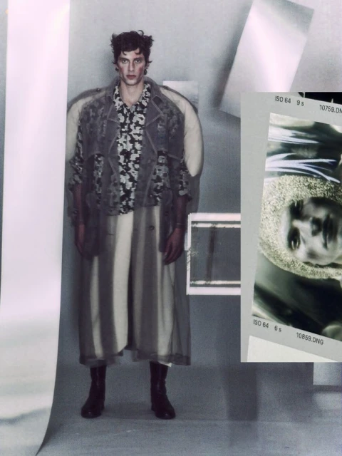 Editorial fashion shot of a male model posing in a floral shirt, long coat, boots, and abstract background with geometric shapes.