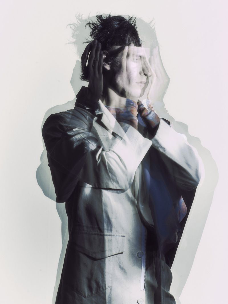 Conceptual portrait of a male with hands near his face, wearing a blazer against a bright background, utilizing a multiple exposure technique.