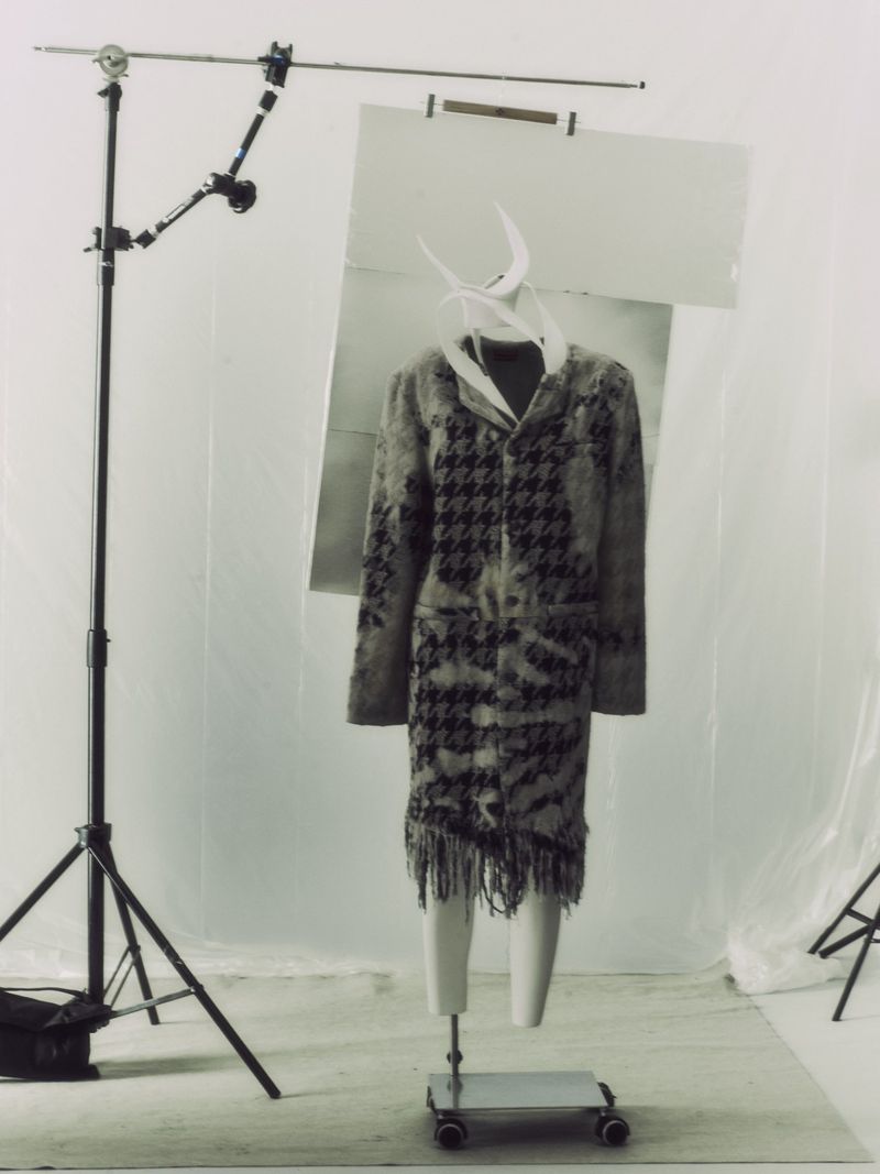 Fashion shot of coat with houndstooth pattern on mannequin in photo studio setting, lit by studio lights and with background screen.