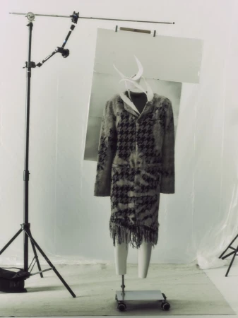 Fashion shot of coat with houndstooth pattern on mannequin in photo studio setting, lit by studio lights and with background screen.