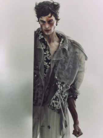 Portrait of a male model with an injured face in a gray jacket and patterned shirt against a plain white background, studio shot.