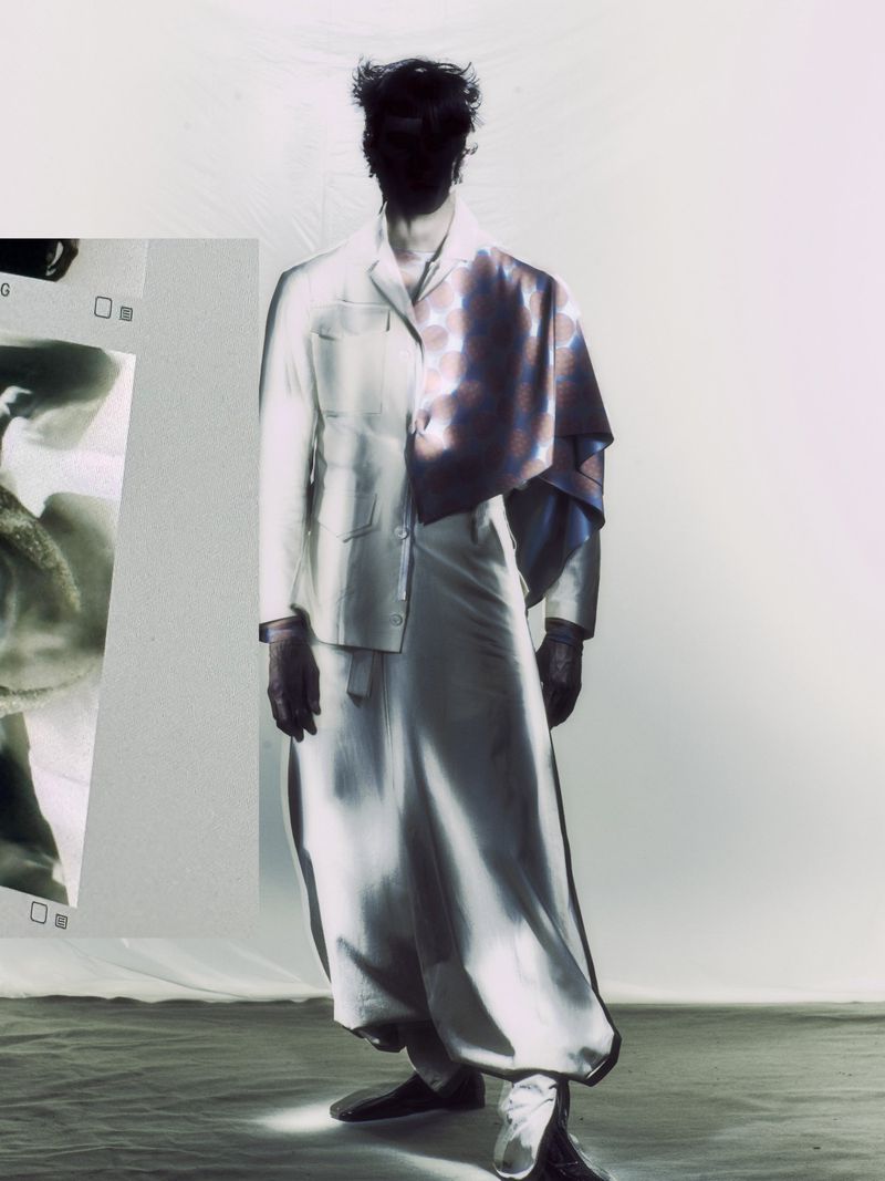 Man stands in a photo studio wearing a pale suit with purple cloth draped over shoulder, obscured face, surreal and artistic image.