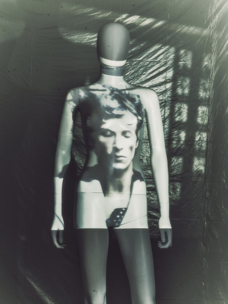 Mannequin with face projection stands in a photo studio with lighting and shadow play, creating an artful, monochrome fashion-forward visual.