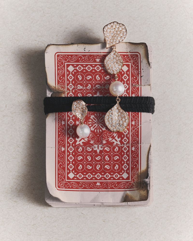 Elegant drop earrings featuring pearls and shimmering details displayed on a stack of playing cards, creating a unique and luxurious presentation.