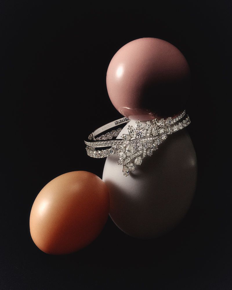 Elegant diamond bracelet resting on a white egg, next to a pink egg on a stark black background, jewelry still life.