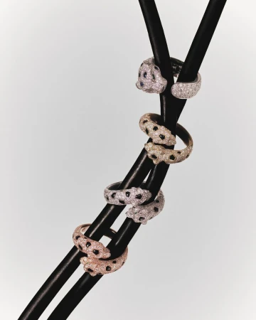 Close-up of diamond and gemstone panther rings coiled around a black metal structure against a light gray background, jewelry product shot.