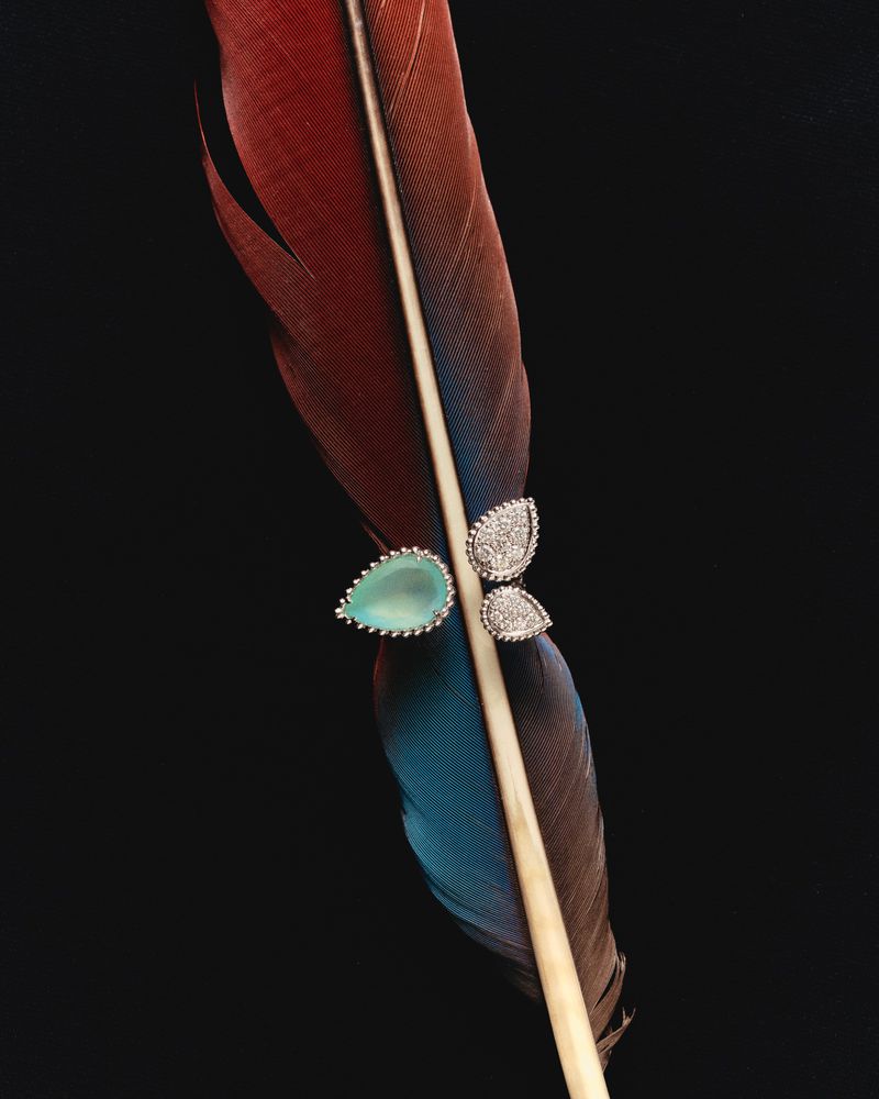 Elegant jewellery with teardrop aquamarine stone and diamond accents on a red and blue feather against a stark black backdrop.