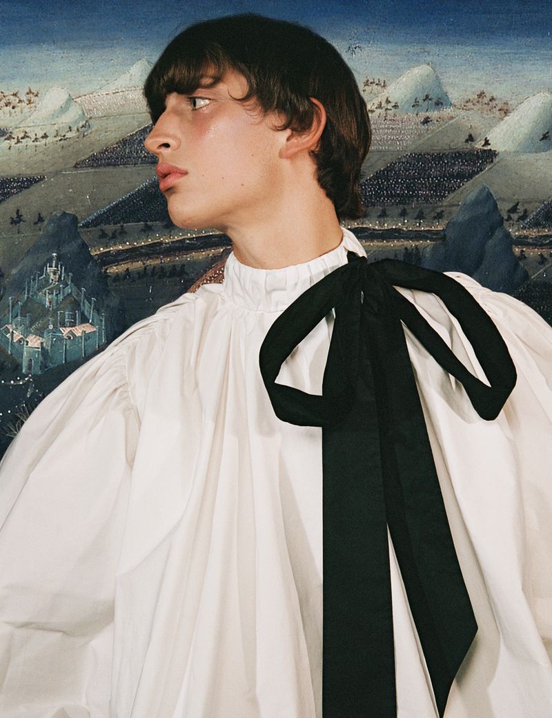 Portrait of a fair-skinned person in a white blouse with a large black bow, set against a backdrop of a scenic landscape painting.