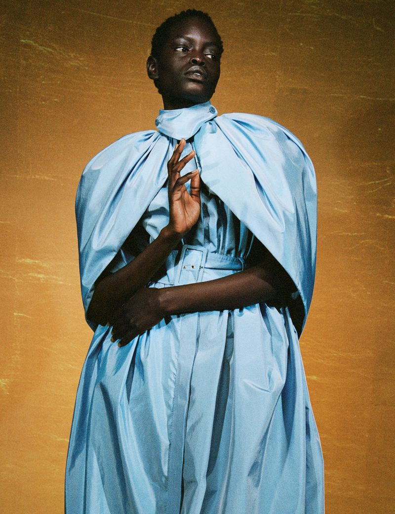 Elegant portrait of a Black woman in a light blue gown against a textured gold background, showcasing fashion and beauty.