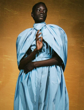 Elegant portrait of a Black woman in a light blue gown against a textured gold background, showcasing fashion and beauty.
