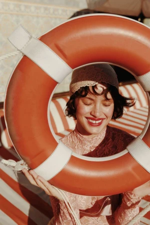 Woman in lace dress and hat framed by orange life preserver with red and white striped background in a close-up eye-level outdoor shot.