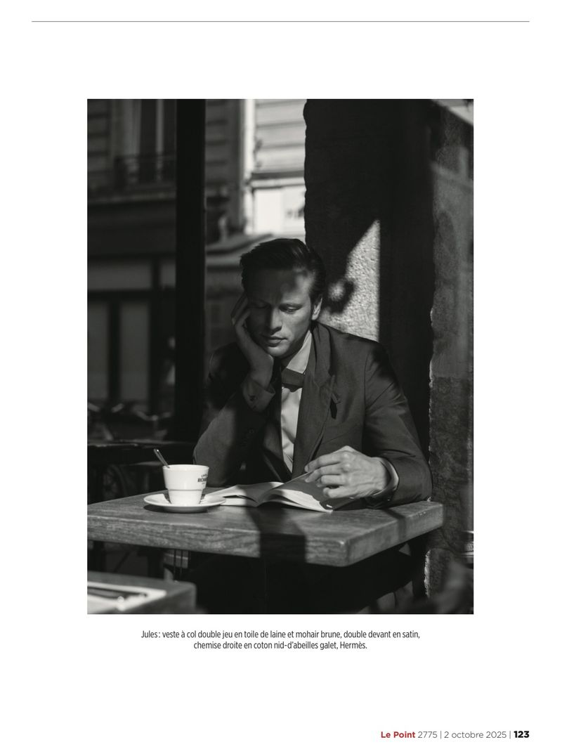 Black and white photograph of model Jules Raynal seated at an outdoor cafe table reading with a coffee cup.