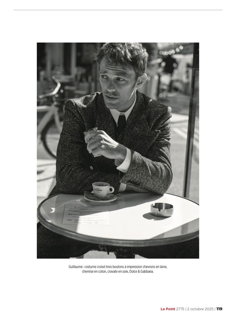 Model Guillaume Babouin seated at an outdoor café table wearing a herringbone jacket with an espresso cup and ashtray.