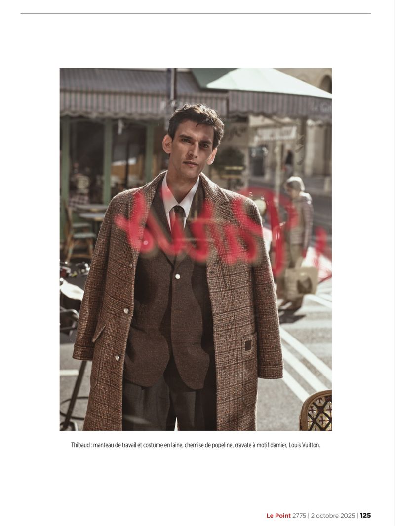 Fashion shot of a man in a suit and tweed overcoat standing in front of a cafe with a passerby. Focus on elegant attire.
