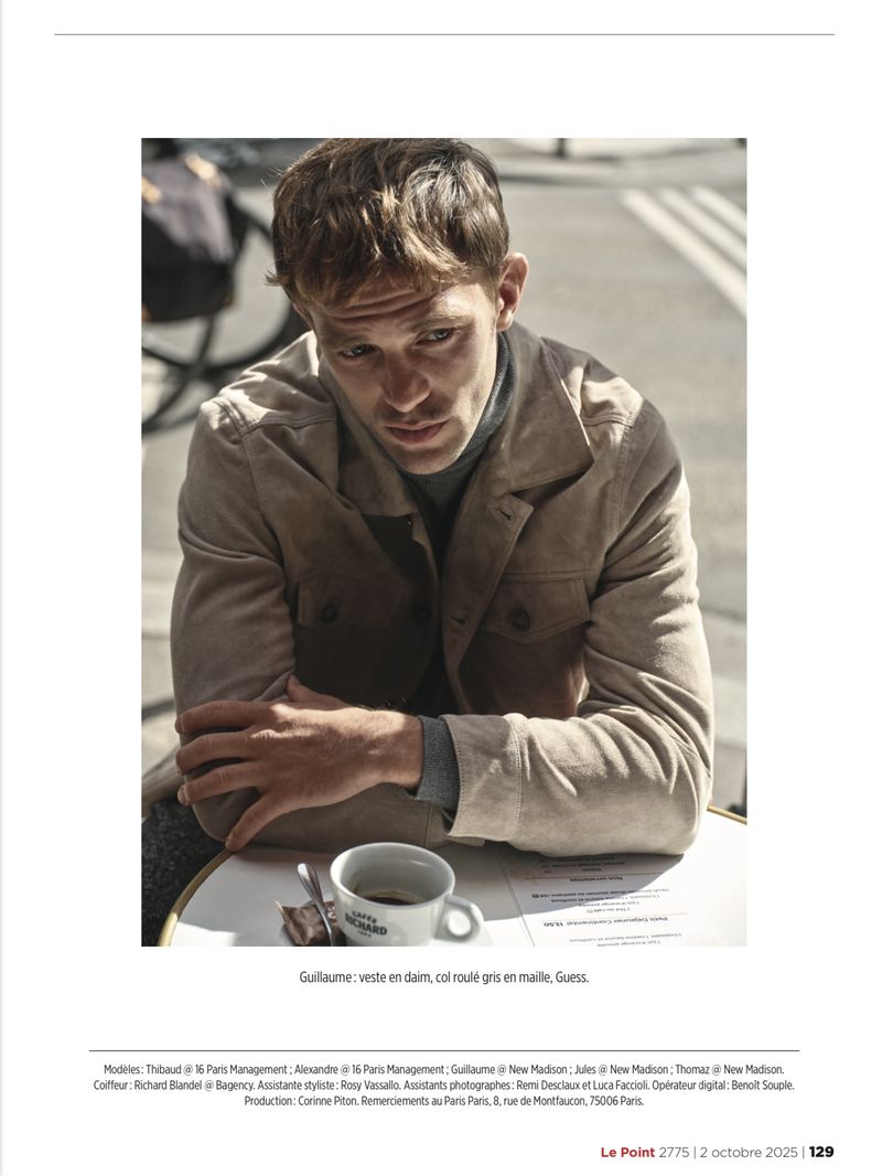 Portrait of a man at a cafe table with a coffee cup, wearing a grey jacket and turtleneck, showcasing fashion and lifestyle.