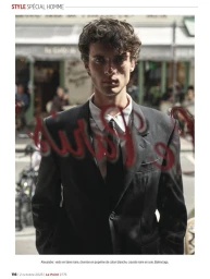 Model Alexandre Tardivel in a black Balenciaga suit and tie photographed through a window with red lettering in Paris.