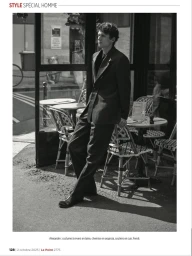 Model Alexandre Tardivel leans against bistro chairs outside a café in a dark tailored suit for a Le Point menswear editorial.