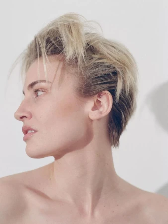 Headshot of a light-skinned woman with blonde hair looking away from the camera in front of a white background in a photo studio.