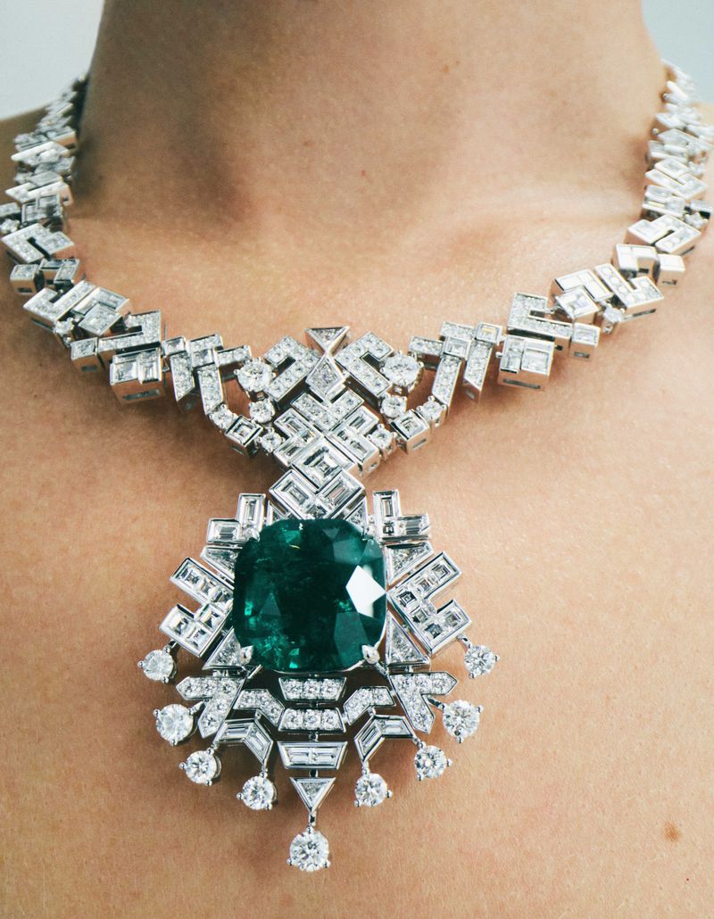 Close-up studio shot of a woman's bare chest and neck adorned with a lavish white gold and emerald pendant diamond necklace.
