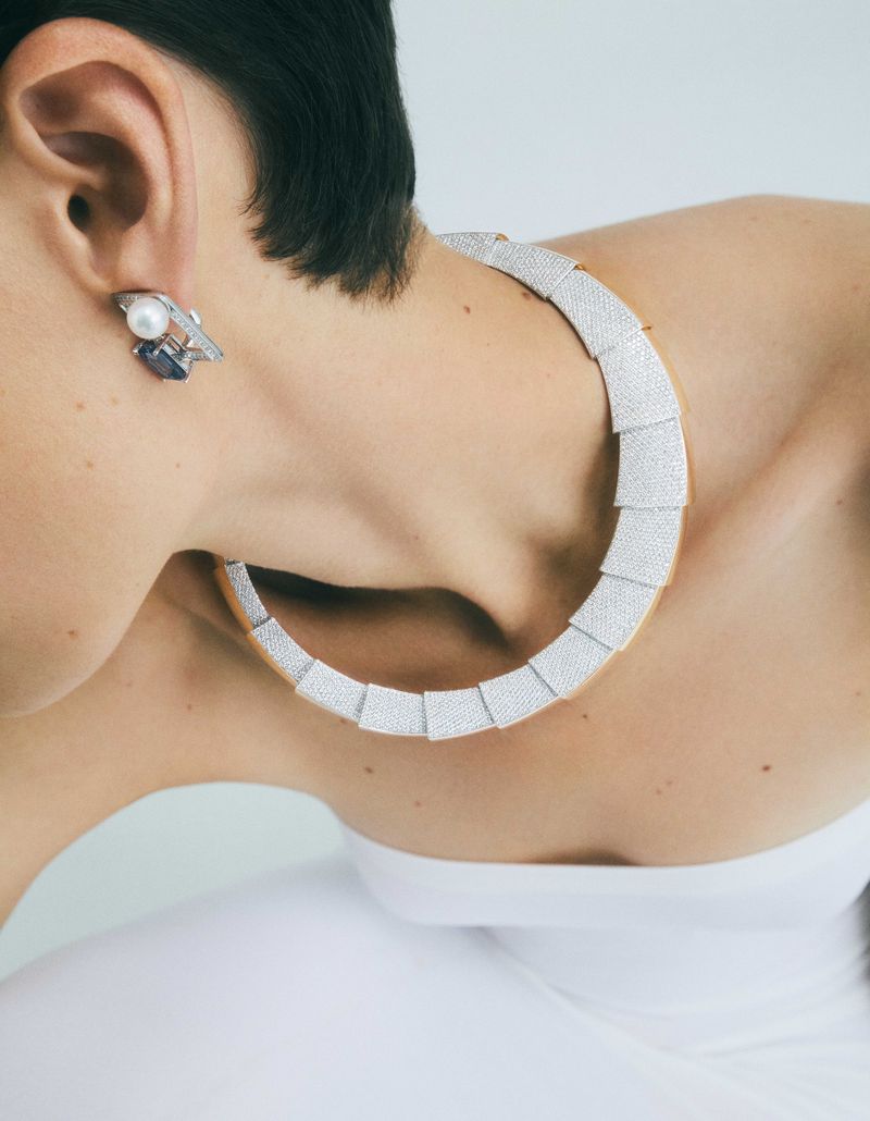 Adult female model showcases a silver necklace and earring jewelry set against a neutral backdrop in a close-up studio portrait.