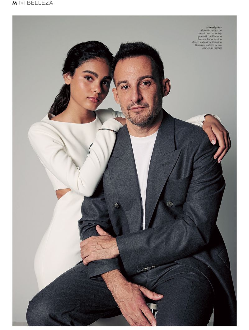 Portrait of a man in a dark grey suit and a woman in a white dress posing together against a plain grey backdrop.