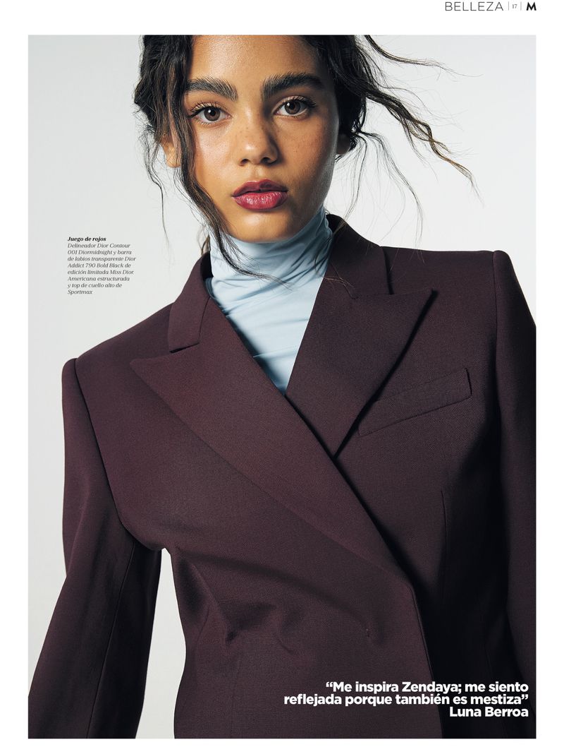 Luna Berroa wearing a deep burgundy blazer over a light blue turtleneck against a white studio background.