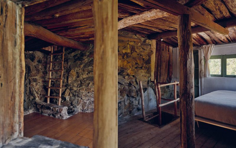 Interior view of rustic cabin features stone walls, exposed wooden beams, and a wooden ladder leading to a loft space.