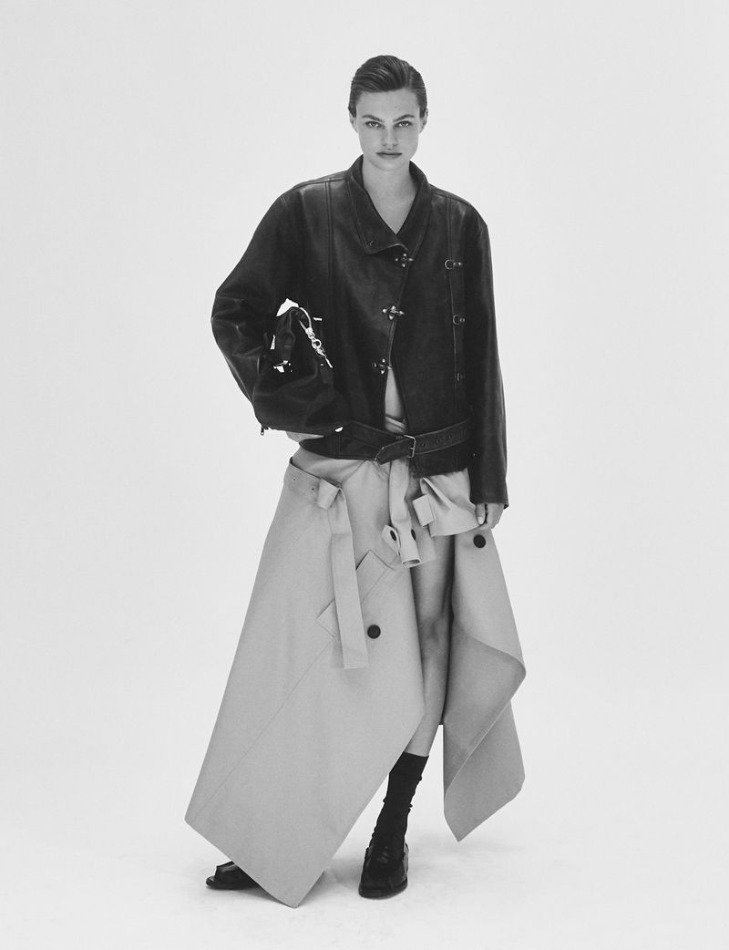 Model Anne Boomgaart wearing a black leather jacket and an asymmetrical beige skirt against a white seamless background.