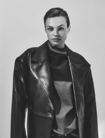 Portrait of a woman with short hair wearing a black leather trench coat in a studio setting. The image is black and white.