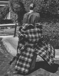 Back view of model Anne Boomgaart wearing an oversized belted plaid coat on a street in black and white.