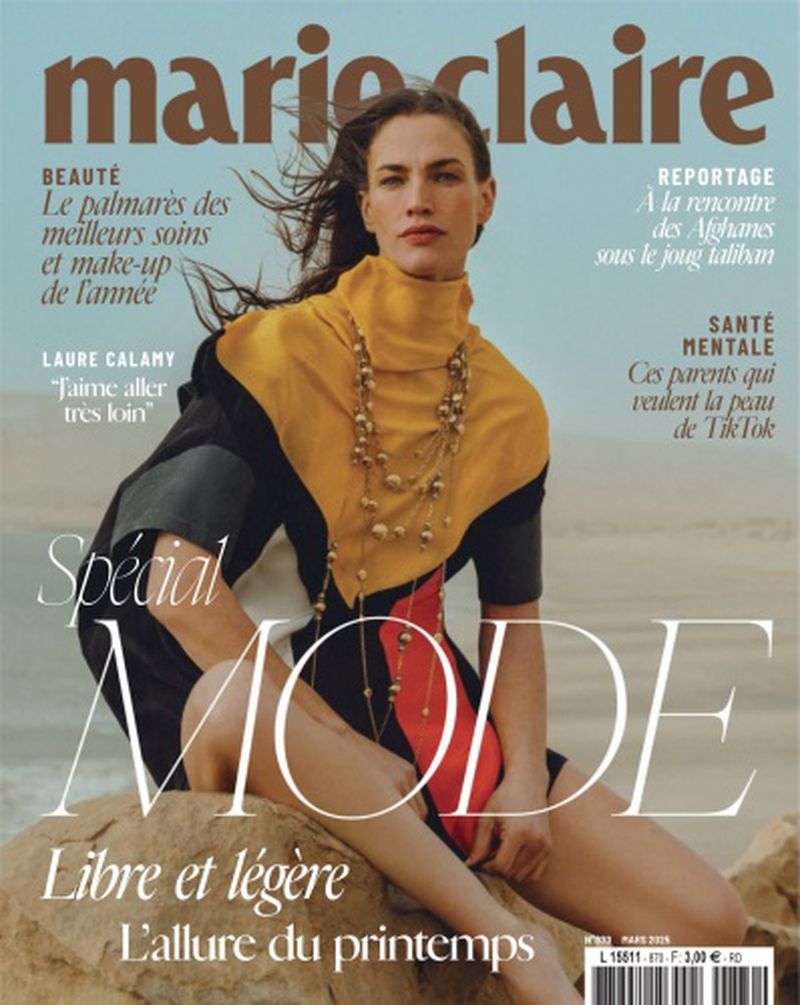 Marie Claire cover featuring a woman in a yellow and black dress sitting on a rock with a desert and light blue sky background.