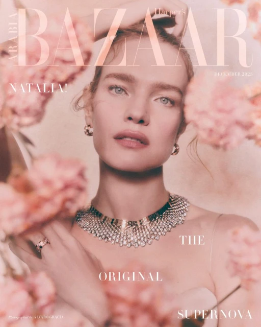 Close-up of an adult woman with light skin and blue eyes wearing jewelry, pink flowers framing her face and shoulders, magazine cover.
