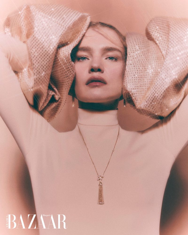 Fashion editorial portrait of a blonde woman wearing a white turtleneck and sequined puffed sleeves, accessorized with a gold necklace.