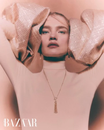 Fashion editorial portrait of a blonde woman wearing a white turtleneck and sequined puffed sleeves, accessorized with a gold necklace.