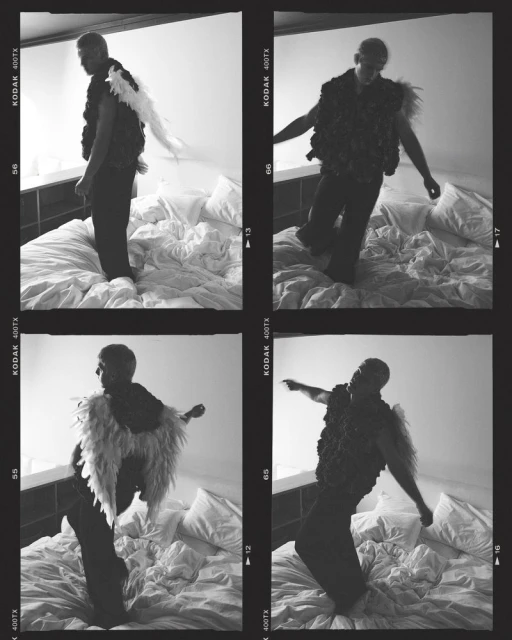Monochrome photo of a man posing on a bed in a vest with wing-like extensions, captured in a film strip style image with grain.