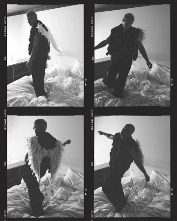 Monochrome photo of a man posing on a bed in a vest with wing-like extensions, captured in a film strip style image with grain.
