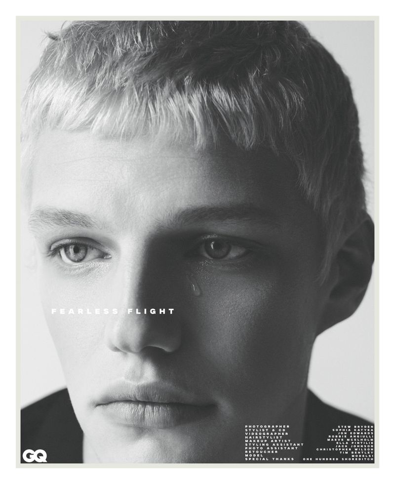 Black and white portrait of a young, light-skinned male with blonde hair and a teardrop on his face, set against a plain backdrop.