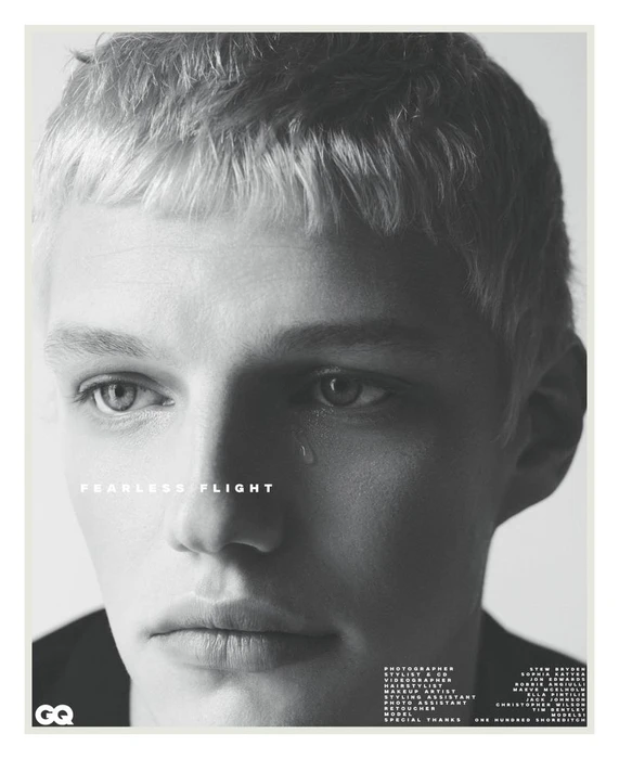 Black and white close-up portrait of a young man with short blonde hair and a single tear on his cheek.