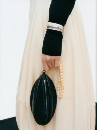 Close-up shot featuring a black handbag, cream-colored skirt, beaded bracelet, and beaded bag strap, set against a minimalist white background.